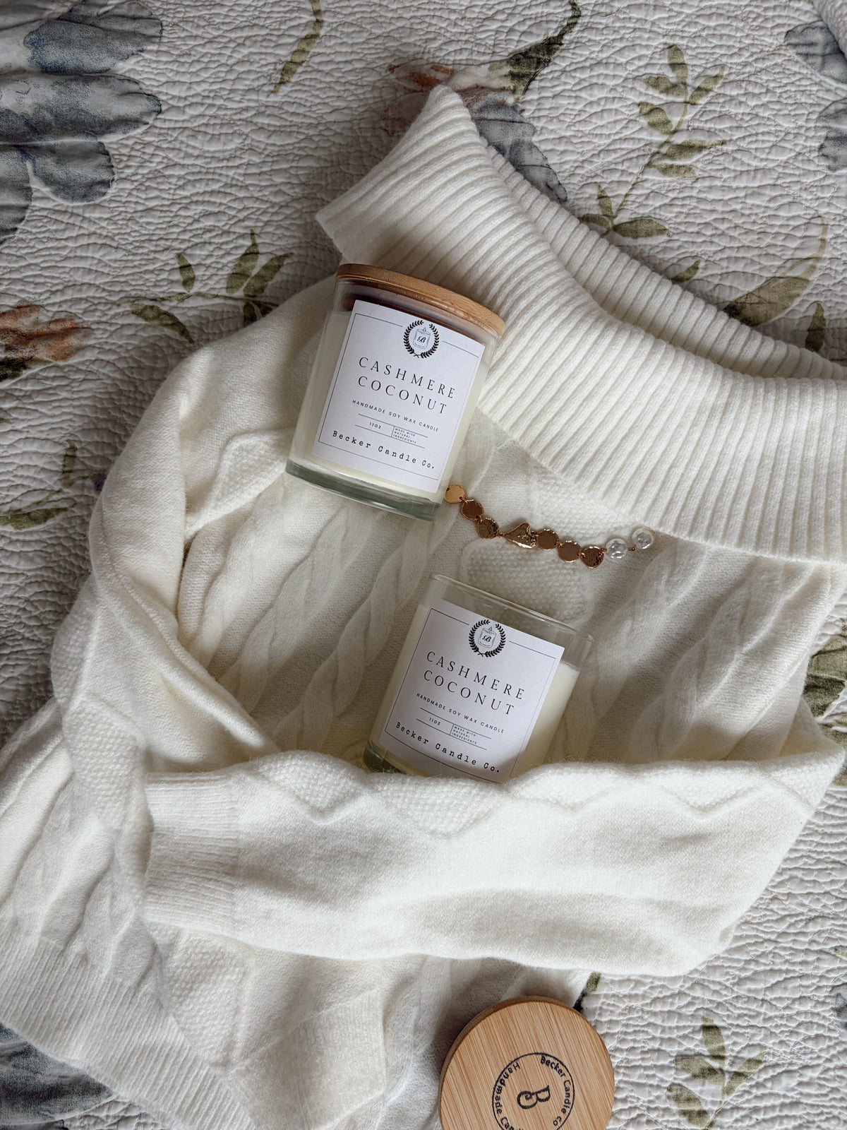 Two Cashmere Coconut candles from Becker Candle Co. resting on a cream knit sweater